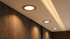 Recessed ceiling lights in a modern room emit soft, warm light. The beige and brown walls enhance a cozy, inviting atmosphere.