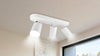Ceiling-mounted white track lighting fixture with three adjustable spotlights, illuminating a room. A modern, minimalistic design creates a bright, airy atmosphere.