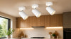 Three white ceiling spotlights illuminate a modern kitchen with wooden cabinetry and a window view.